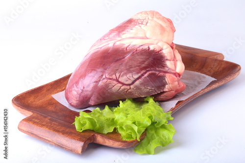 Raw beef heart and lettuce leaf on wooden desk isolated on white background from above and copy space. ready for cooking.