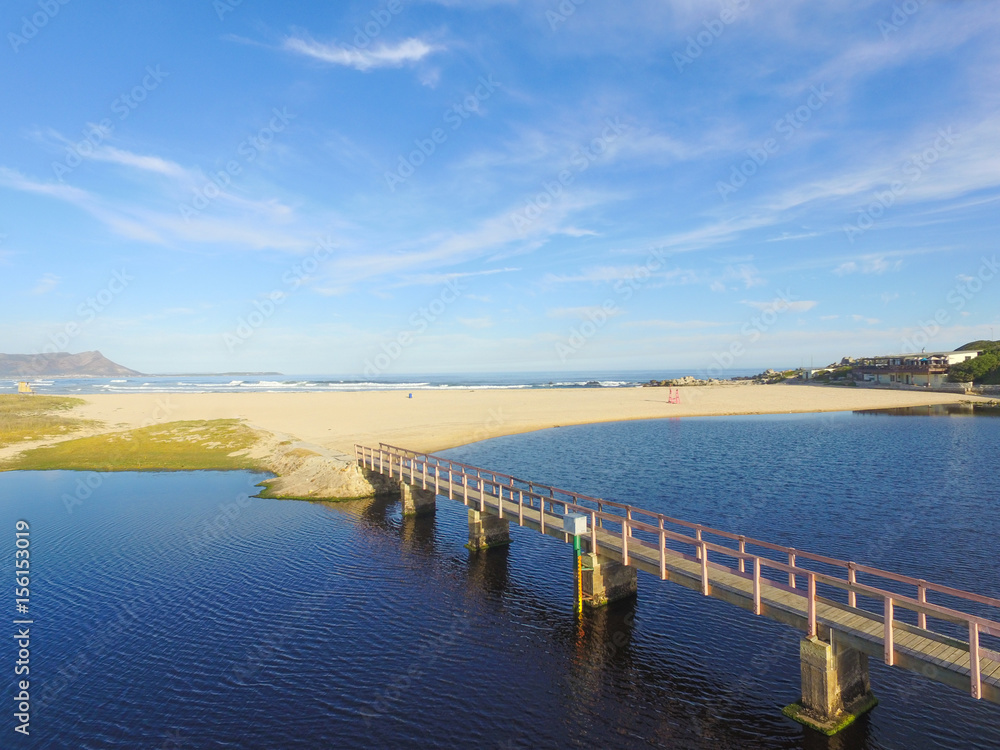 Obraz premium Bridge over the Lagoon to the Ocean with Blue Skies and Clouds