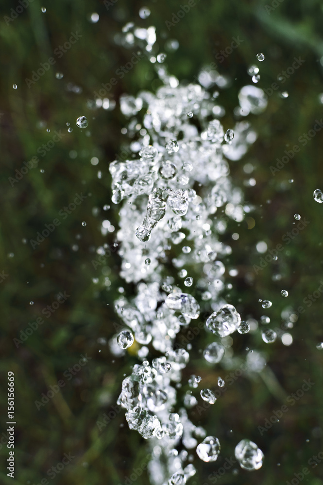 Splashing water in sunlight against a green background, abstraction. Close-up, selective focus. Splashing water in sunlight against a green background, abstraction. Close-up, selective focus.