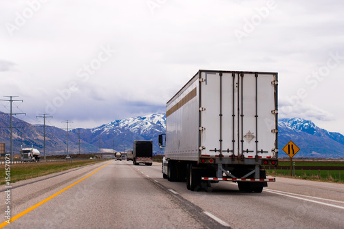 Picturesque straight highway trucks trailers snow capped mountains of Utah