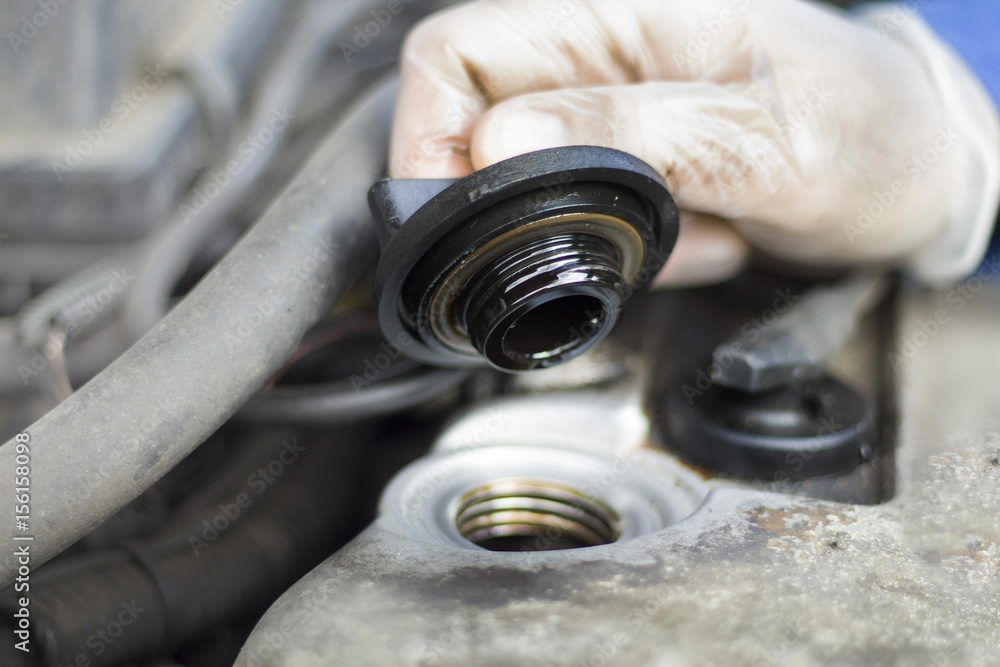 Ręce mechanika samochodowego odkręcają korek wlewu oleju. Mechanik w rękawiczkach jednorazowych odkręcił korek wlewu oleju w silniku. Korek wlewu oleju odkręcony. Ręka trzyma korek. Ręce mechanika samochodowego odkręcają korek wlewu oleju. Mechanik w rękawiczkach jednorazowych odkręcił korek wlewu oleju w silniku. Korek wlewu oleju odkręcony. Ręka trzyma korek.