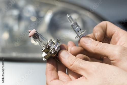 Dłonie mechanika trzymają żarówki samochodowe H1 i H7. Mechanik wybiera żarówkę do samochodu H1 czy H7. Rodzaje żarówek samochodowych H1, H7