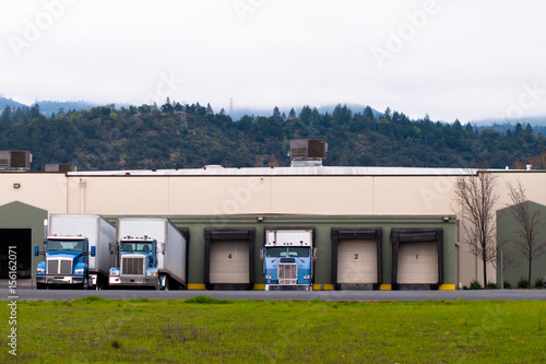 Semi trucks blue trailers loading unloading cargo in warehouse building gates doors © vit
