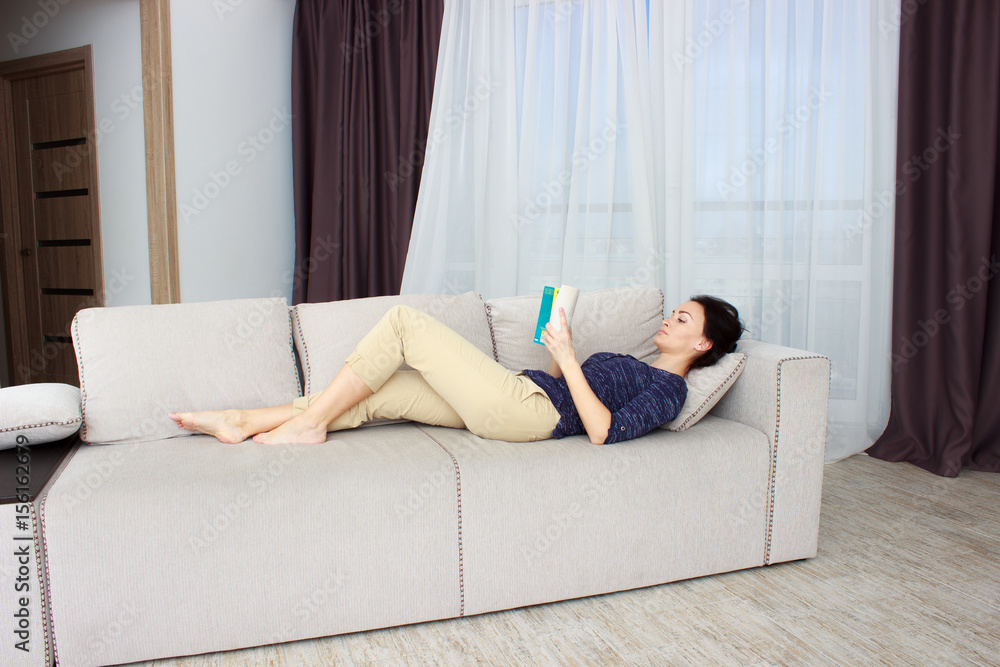 Beautiful young woman reading magazine and lying on sofa at home Beautiful young woman reading magazine and lying on sofa at home