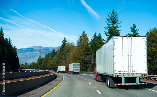 Obraz na plátně Convoy Semi trucks dry van trailers on winding highway interstate I-5 back view