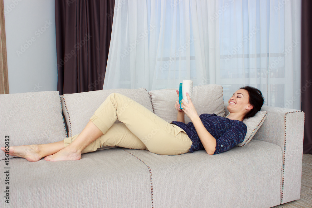 Smiling beautiful brunette relaxing on the couch and reading a book in the living room Smiling beautiful brunette relaxing on the couch and reading a book in the living room