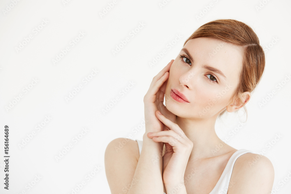 Portrait of young beautiful girl looking at camera touching face over white background. Facial treatment. Beauty cosmetology and skincare.