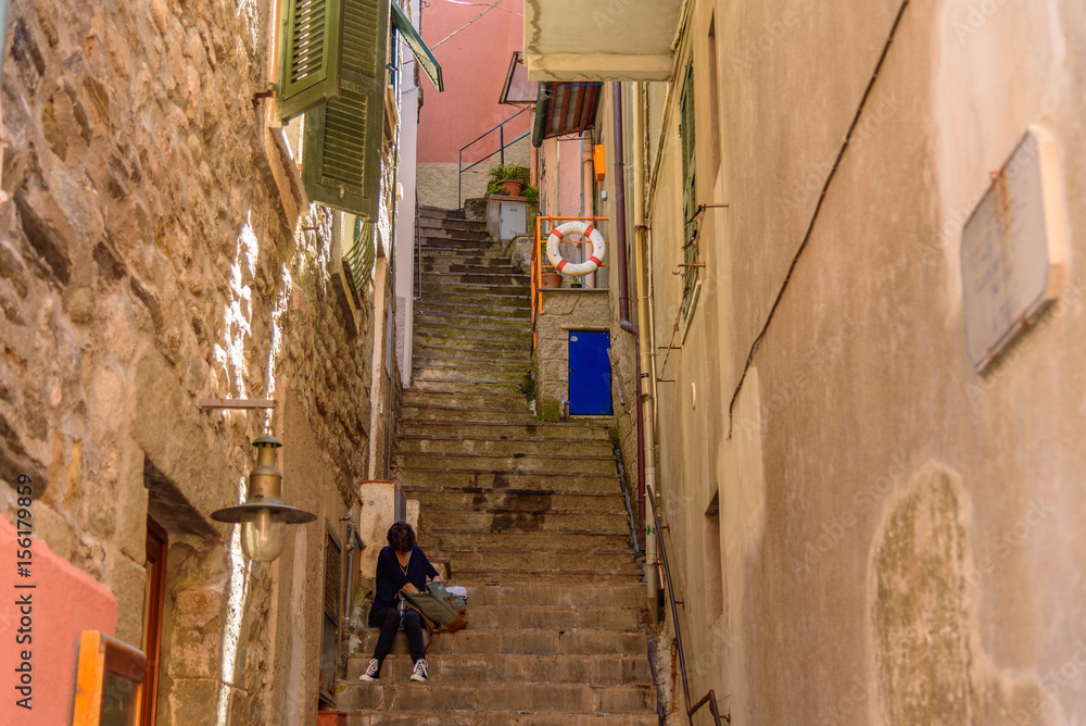A tourist looks in his bag sitting on a stairway in Manarola, Liguria, Italy