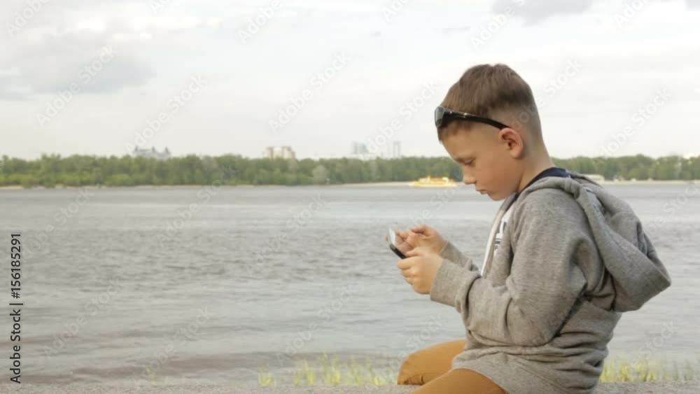 A boy is playing on a tablet near the sea A boy is playing on a tablet near the sea