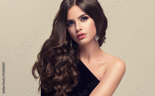 Brunette girl with long and shiny wavy hair . Beautiful model with curly hairstyle .