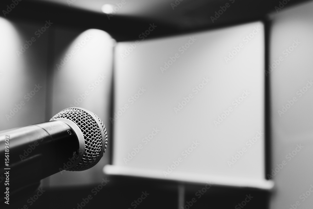 Obraz premium microphone ready to use in the podium and the projector screen on the back of the meeting room for the press conference. selective focus. black and white photo.