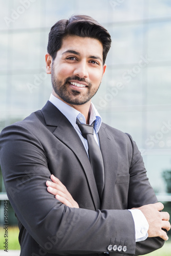 Smiling businessman or worker standing in suit near office building