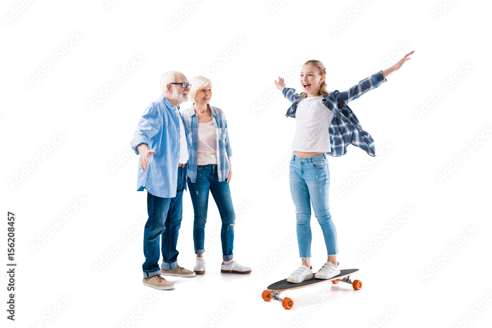 Obraz premium grandfather, grandmother and happy granddaughter with skateboard isolated on white