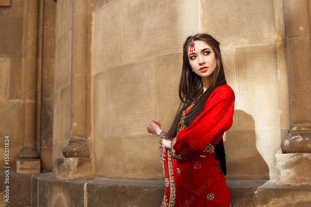 Indian bride in red sari poses before stone wall outside