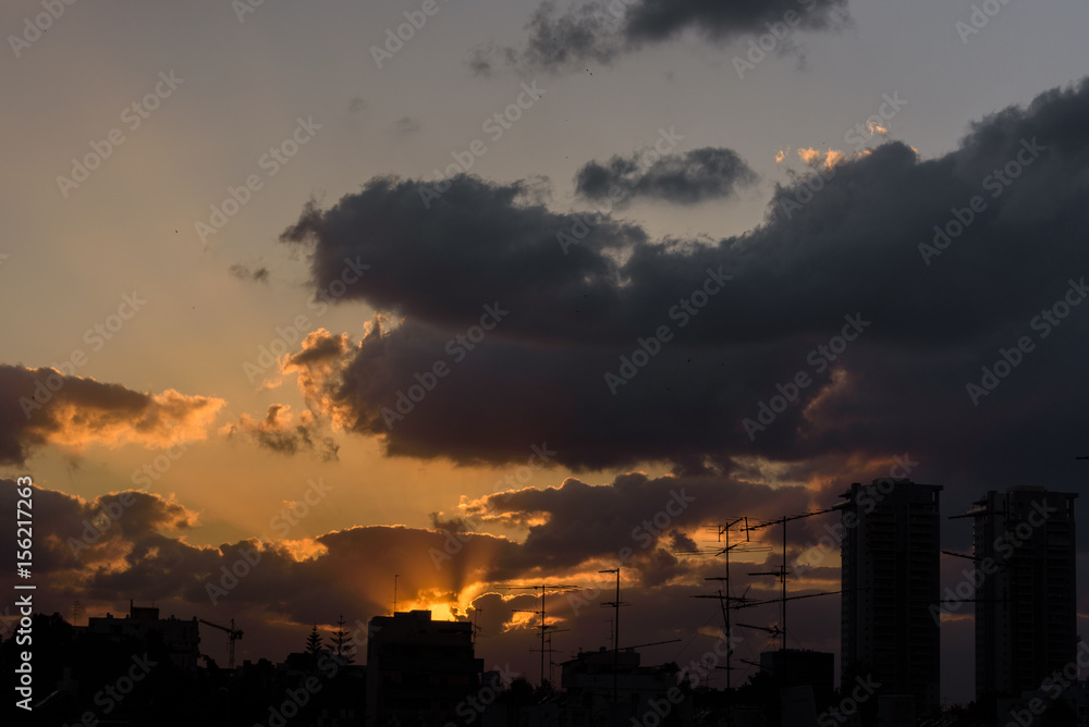 Sun sets behind clouds still revealing skyline of town - Petach Tikva, Israel