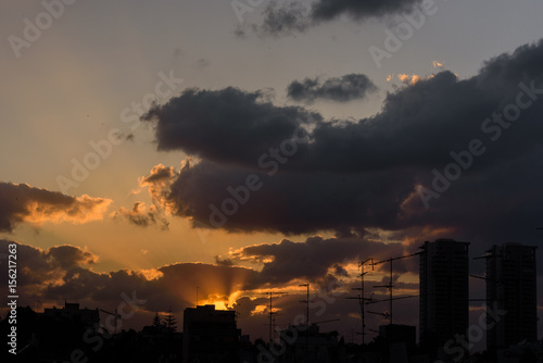 Sun sets behind clouds still revealing skyline of town - Petach Tikva, Israel