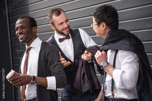 young multiethnic businessmen in formalwear talking at coffee break outdoors, business team meeting