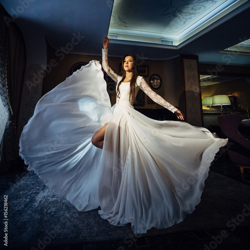 The charming girl has a white dress and stands in the room photo