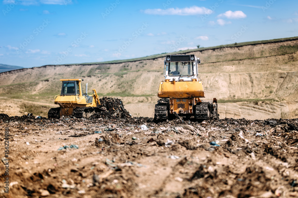 Yellow mini bulldozers working and moving garbage on dumping site Yellow mini bulldozers working and moving garbage on dumping site