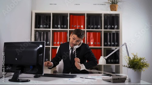 4k uhd. Young successful businessman working hard at office talking mobile and doing many deals typing keyboard of PC. He looks hurry not managed in time . Glidetrack slider cinematic shooting.