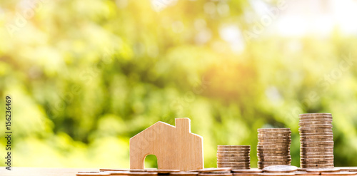 Tableau sur toile wooden house model and coins stacks on table, nature background, money, saving a