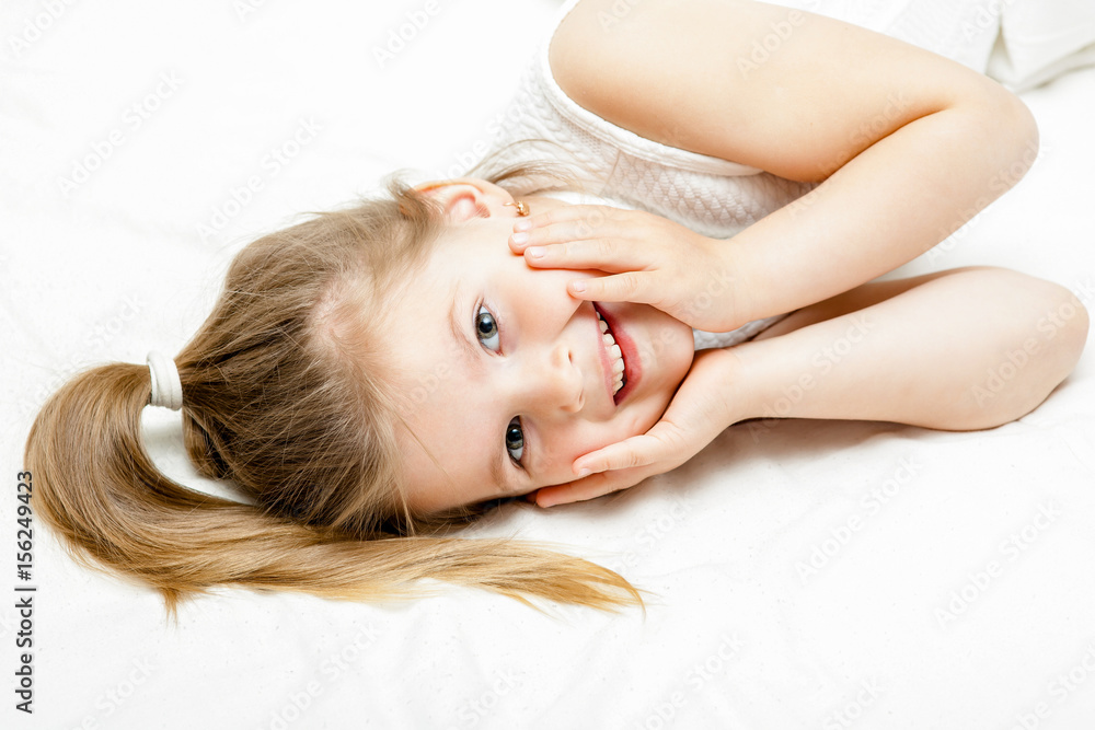 Pretty little blonde girl summer white dress lying on the floor and smiling at camera on white background. Pretty little blonde girl summer white dress lying on the floor and smiling at camera on white background.