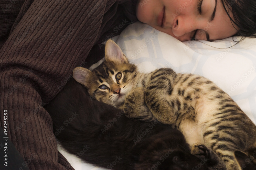 Young brunette woman resting with cute kittens on the bed.