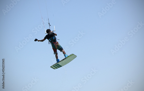 Kite boarding sportsman flying high with kite and kiteboard in boots in the blue sky, active sports and life style, recreation hobby and fun, rider man isolated on the simple air background