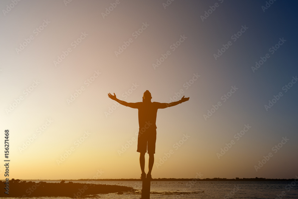 Silhouette man with hands rise up,standing on peak open arms on the pillars at the river, enjoying nature the sun concept world wisdom fun hope