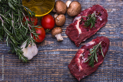 Raw Beef Steak, salt, pepper, garlic, rosemary, olive oil on the black board, background.