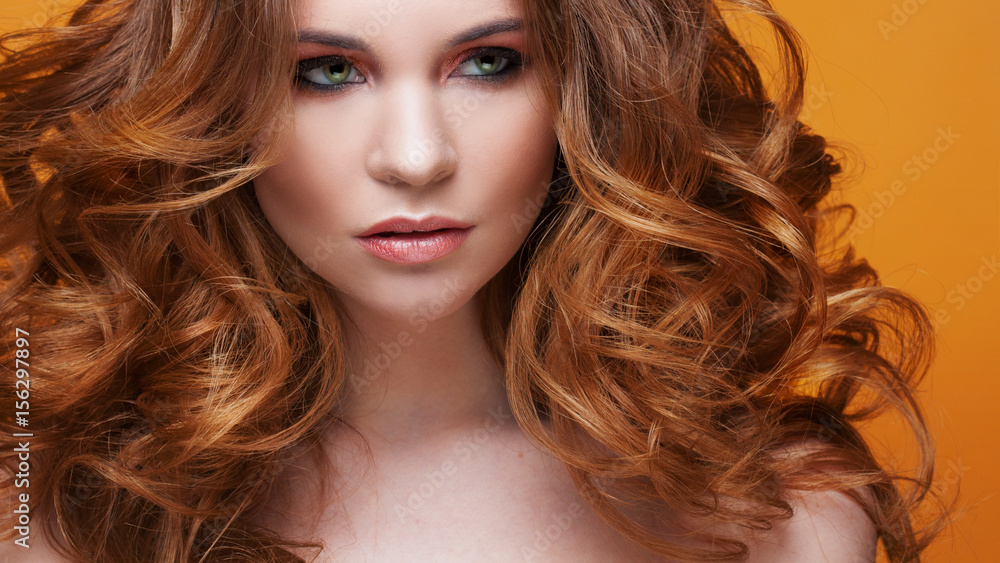 Obraz premium Beautiful redheaded girl with luxurious curly hair. Studio portrait on yellow background. Excellent hair
