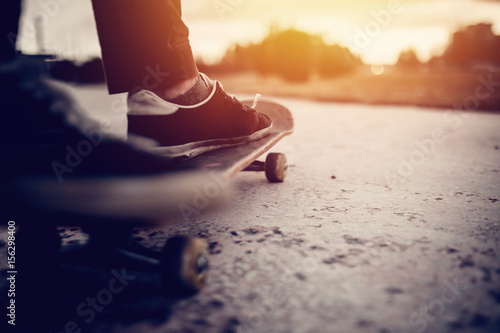 A boot of a skateboarder's shoes is standing on a skateboard ride in the sunset on the road, close-up. Concept street sports in leaky boots