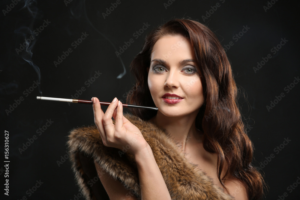 Obraz premium Beautiful woman smoking cigar on dark background
