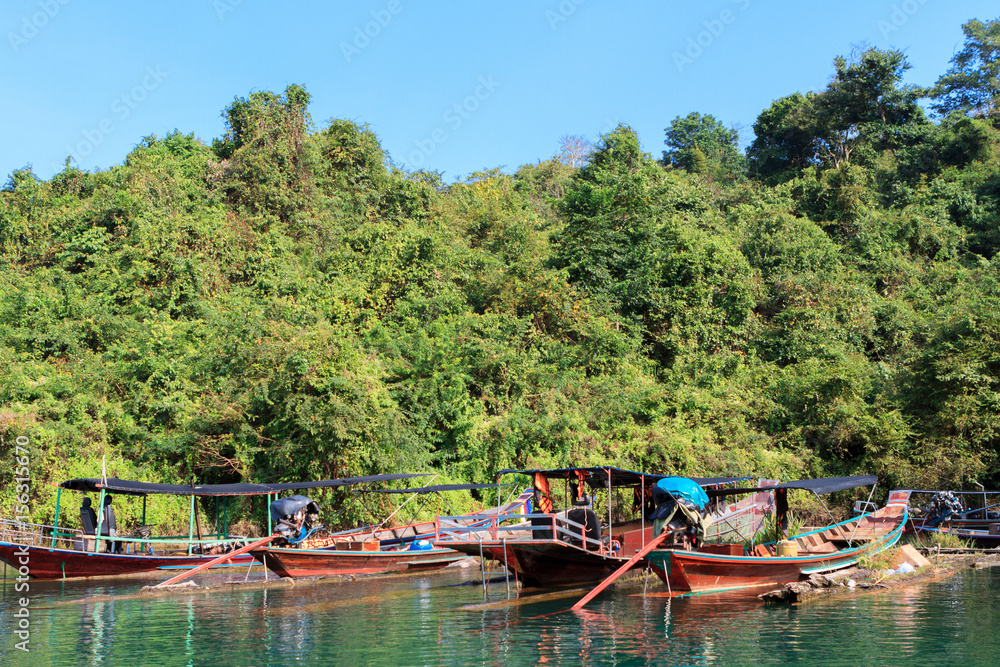 Traditional Thai fishing boat, anchored on a river, with surrounding jungle.