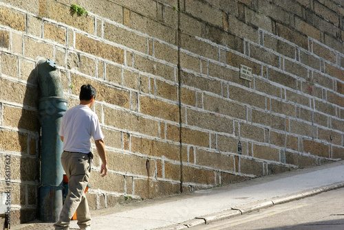 a man walking up a road with brick wall in sunshine