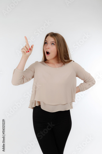 Closeup of cute blonde woman standing on white background. Young woman looking up and pointing at cealing photo
