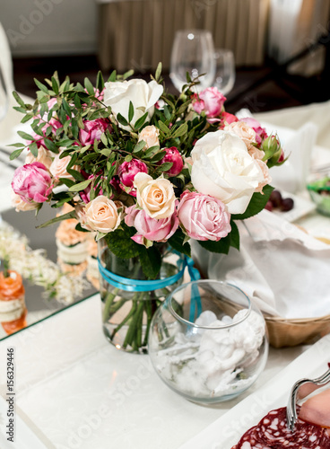 Beautiful wedding bouquet of cream and pink roses in glass vase on dinner table, selective focus. Table setting at a luxury wedding reception. Flowers on the table © mirage_studio