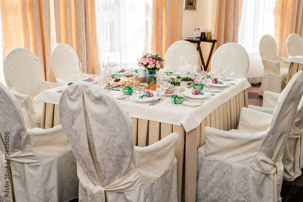 Chairs with white cloth and table for guests served for wedding banquet with flowers. Dinner table for wedding banquet