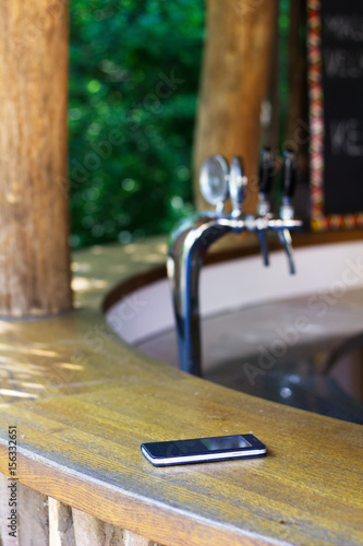 Someone lost a cell phone in a garden pub. Forgotten smartphone on a bar counter in the  outdoor restaurant. Beer draft in a background. 