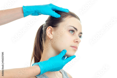 young girl without makeup at a doctor who holds her face in blue gloves close-up