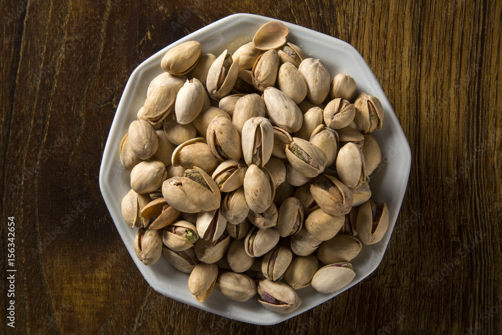 pistachio nuts in white bowl with wood background. pistachio nuts in white bowl with wood background.