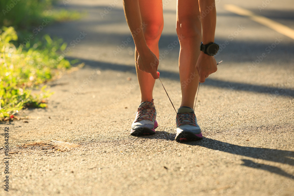 Young fitness woman runner tying shoelace on morning tropical forest trail