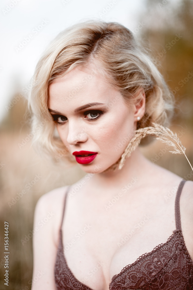 Beautiful and elegant smiling sexy blonde woman with red lips and hair waves wearing beige liingerie posing on the field outdoors summer, retro vintage style and fashion. Beautiful and elegant smiling sexy blonde woman with red lips and hair waves wearing beige liingerie posing on the field outdoors summer, retro vintage style and fashion.