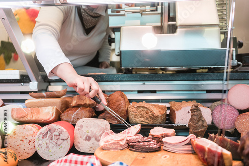Verkäuferin in Fleischerei nimmt Wurst aus der Vitrine zum Verkauf