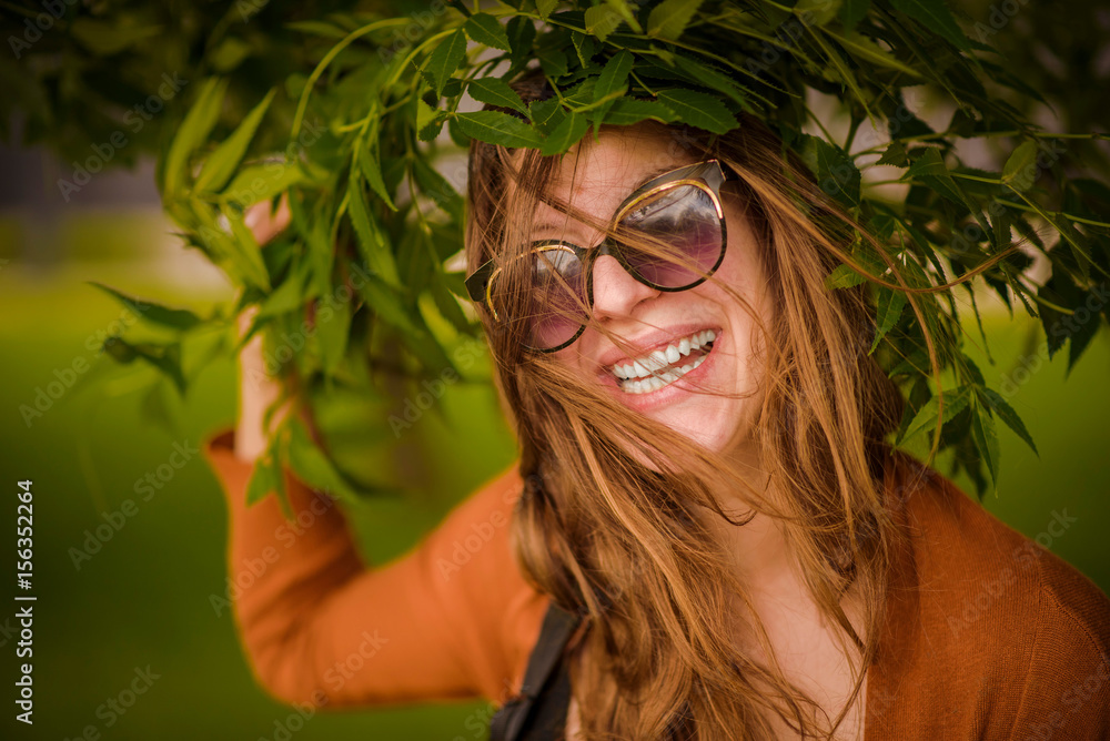 Cheerful young beautiful woman smiling through vibrant green willow branches, enjoying nature and sunny day Cheerful young beautiful woman smiling through vibrant green willow branches, enjoying nature and sunny day