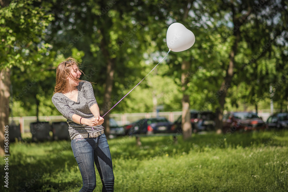 Young attractive woman with a long hair enjoying a sunny day outside, holding a helium balloon, joyful and cheerful