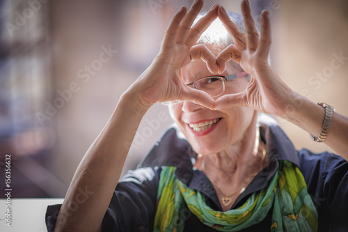 Cute senior old woman making a heart shape with her hands and fingers photo