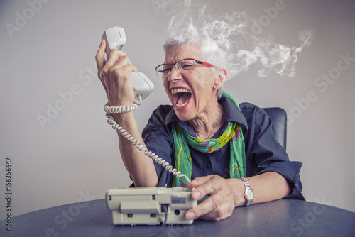 Foto Angry, enraged senior woman yelling at a landline office phone, unhappy with cus