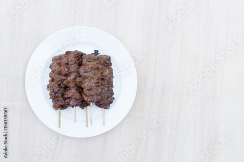Grilled pork with bamboo stick in white dish on wooden background,Thai styled grill pork barbeque