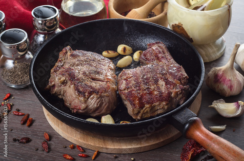 Grilled rib eye steak composition on grill iron pan on wooden background